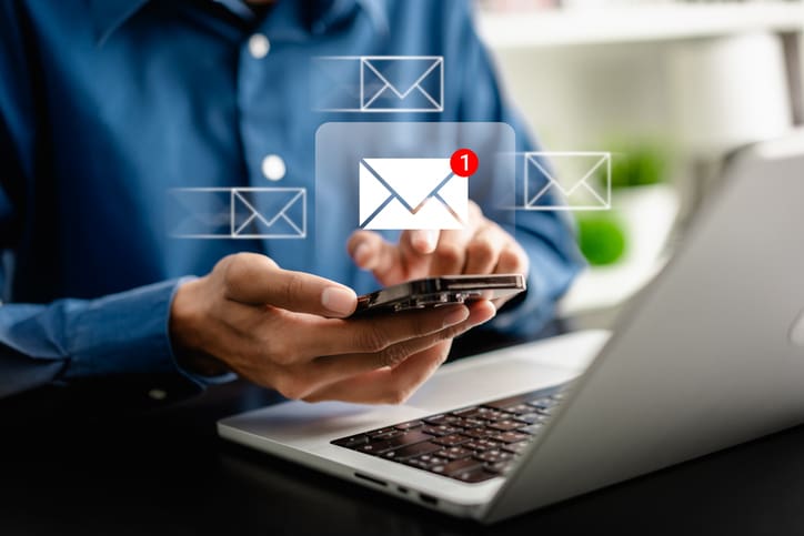 Person holding phone with email notification icons above.