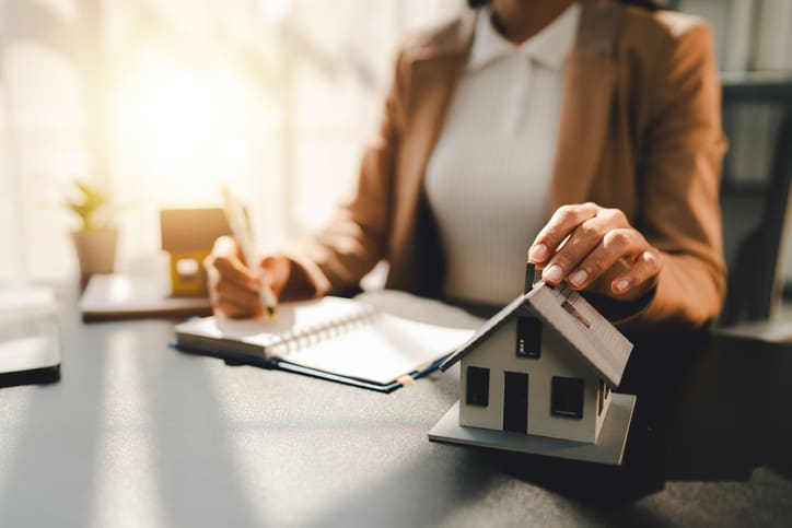 Person signing a document with a small house model on the table.