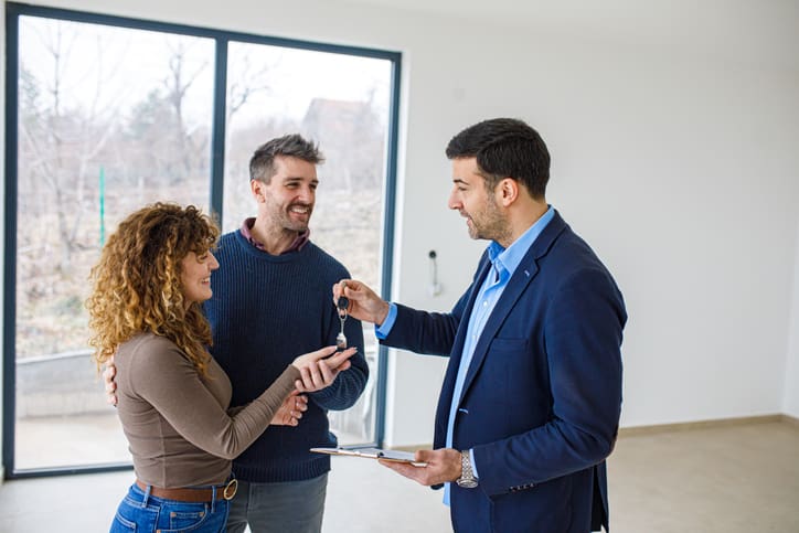 Real estate agent hands house keys to happy couple inside a home.