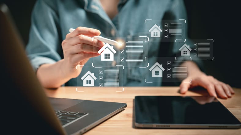 Person using a tablet with floating holographic real estate icons.