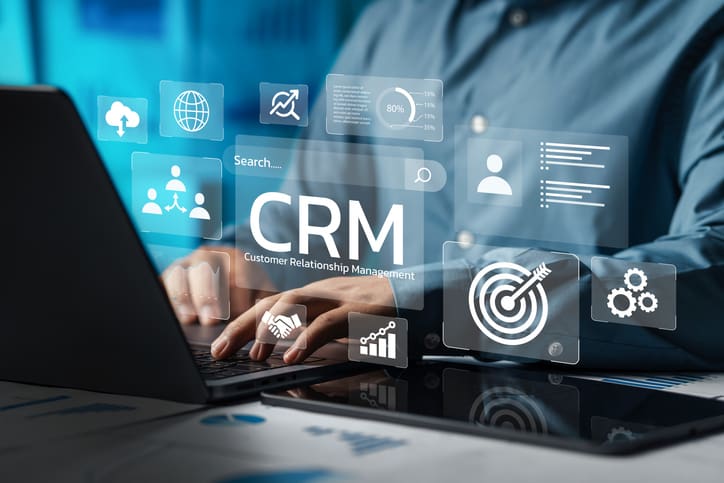 Business professional using CRM software on a laptop with futuristic interface icons.
