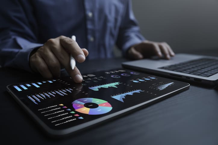 Person analyzing financial data on a tablet with colorful charts and graphs.