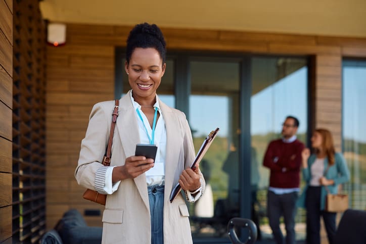A professional woman checks her phone outside an office building.