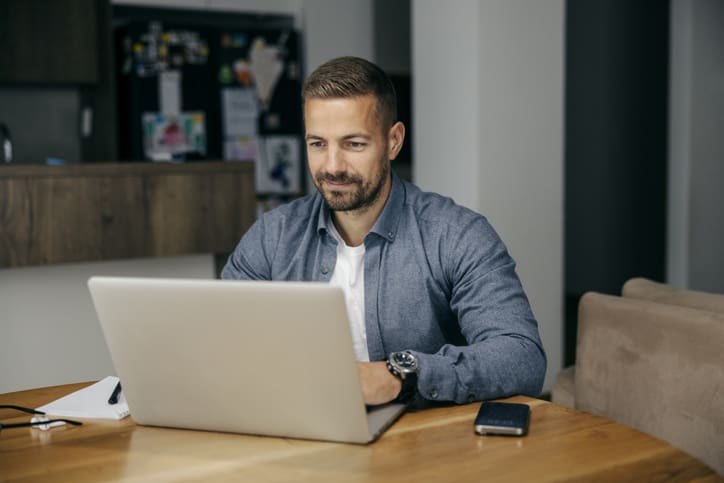 Man working on a laptop at a wooden table.