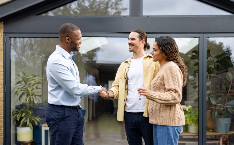 Two men shaking hands while a woman looks on, all smiling.