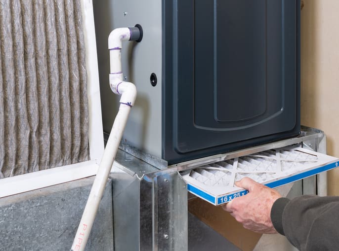 Person applying sealant to a pipe joint near a wall corner.