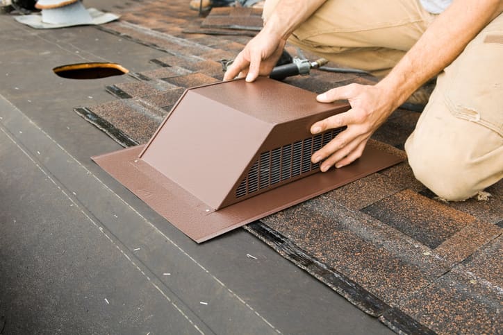 Person installing a brown metal roof vent on shingles.