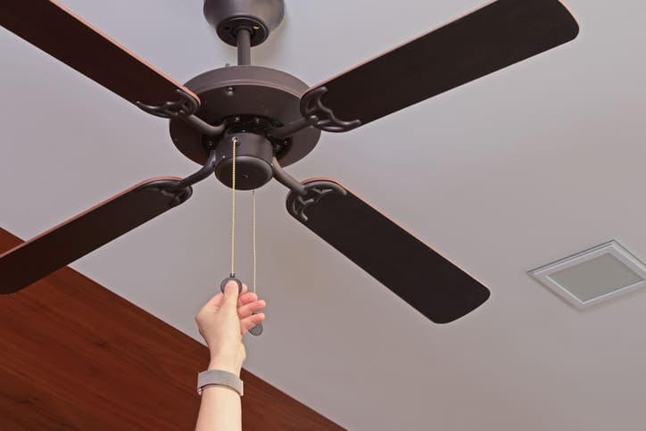 Hand pulling the cord of a ceiling fan.