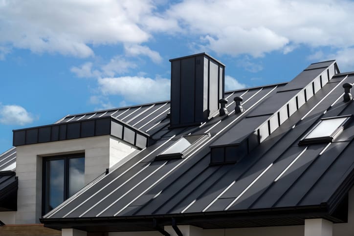 Modern metal roof with a chimney under a partly cloudy sky.