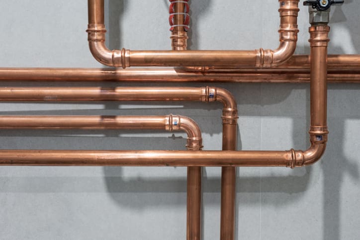 Copper pipes arranged in a plumbing system against a gray wall.