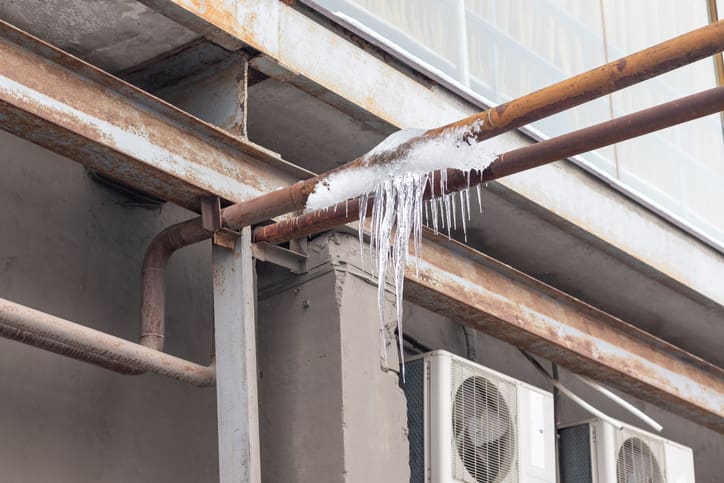 Icicles hanging from a rusty pipe under a bridge.