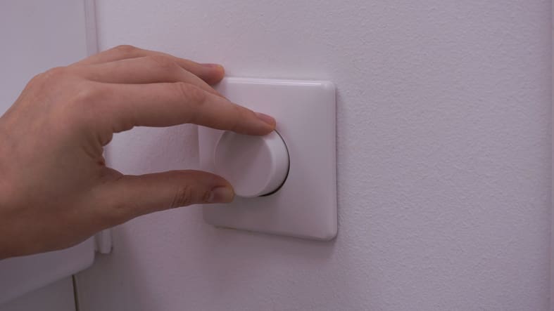 Hand adjusting a white light dimmer switch on a wall.
