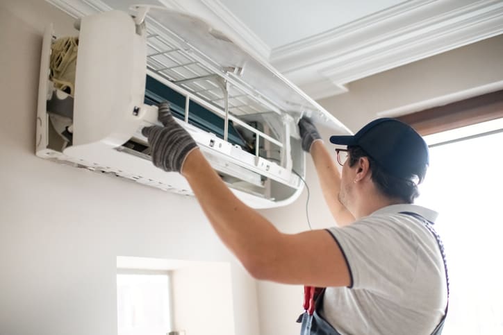 Technician repairing an air conditioning unit indoors.