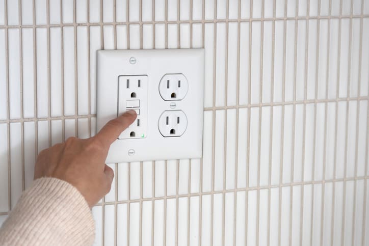 Person pressing a button on a wall-mounted outlet panel.