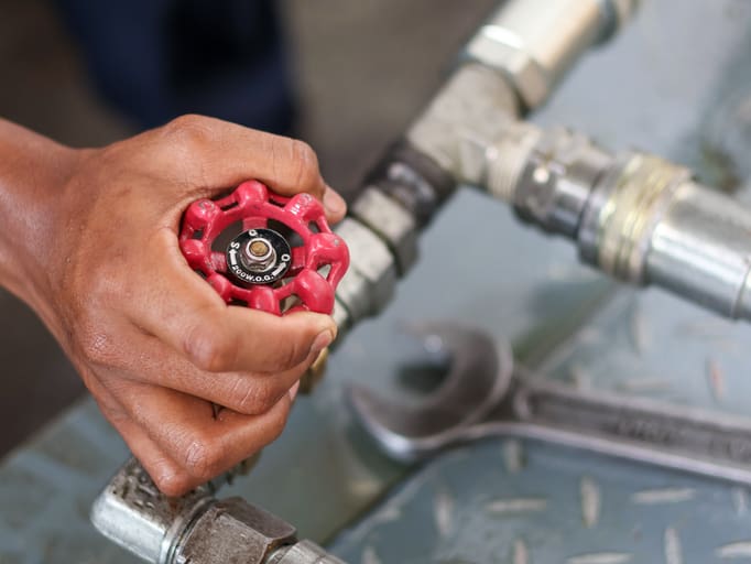 Hand turning a red valve on a metal pipe.