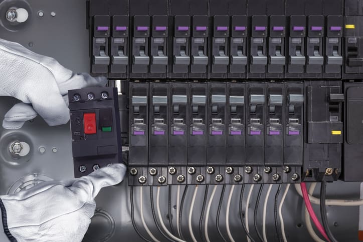 Hand operating a circuit breaker panel with multiple switches and wires.