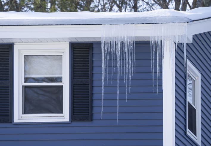 Long icicles hanging from a snowy roof over a window.