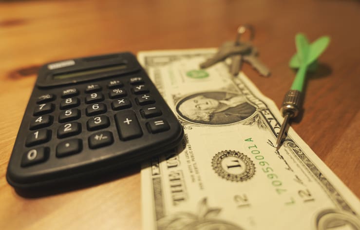 Calculator, dollar bill, keys, and dart on table