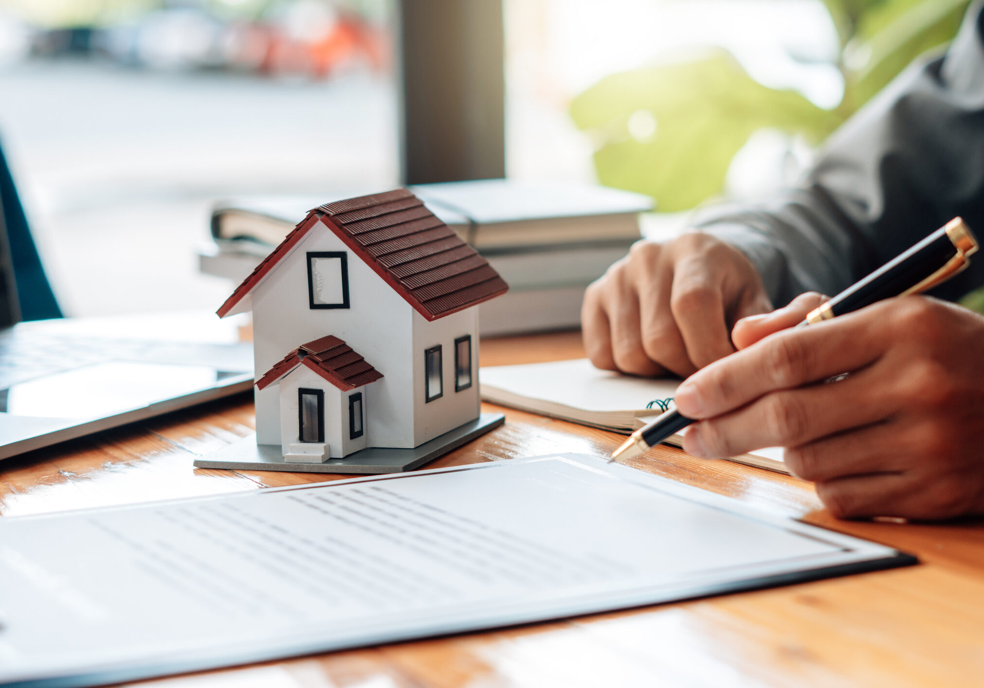 Person signing documents next to small house