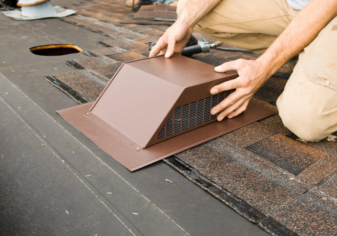 Person installing a brown metal roof vent on shingles.