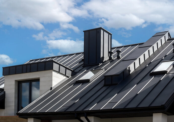 Modern metal roof with a chimney under a partly cloudy sky.