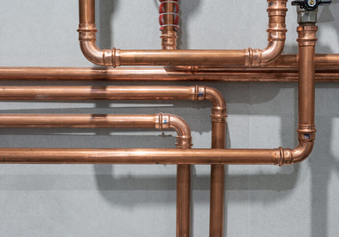 Copper pipes arranged in a plumbing system against a gray wall.