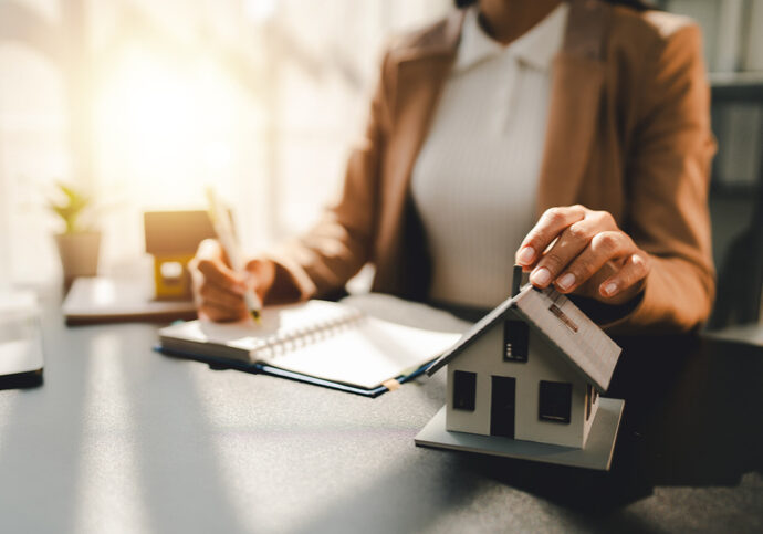 Person signing a document with a small house model on the table.