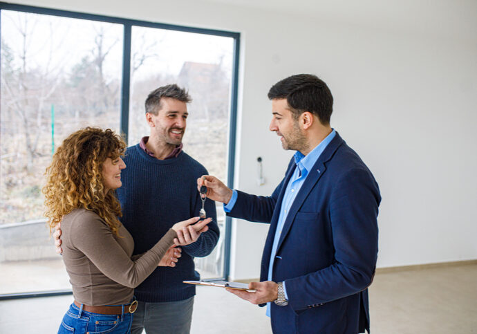 Real estate agent hands house keys to happy couple inside a home.