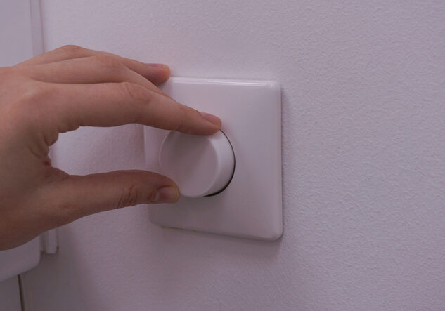 Hand adjusting a white light dimmer switch on a wall.