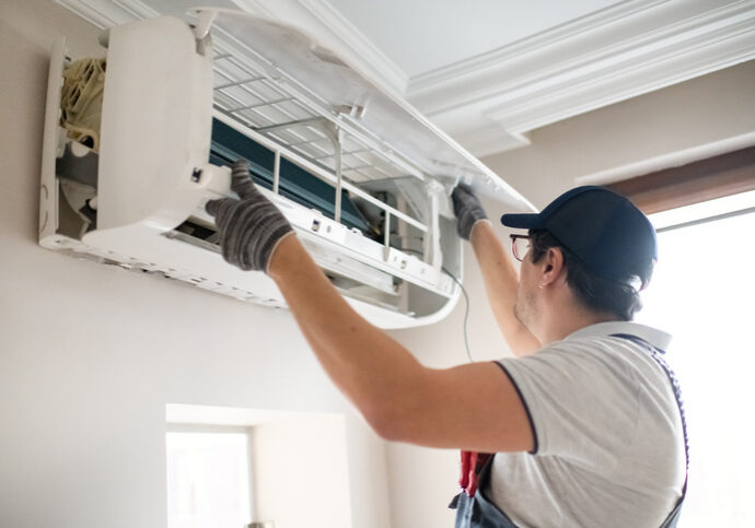 Technician repairing an air conditioning unit indoors.