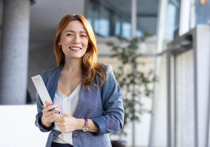 Smiling businesswoman holding rolled-up documents in office lobby.