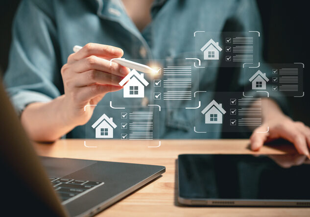 Person using a tablet with floating holographic real estate icons.