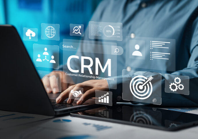 Business professional using CRM software on a laptop with futuristic interface icons.