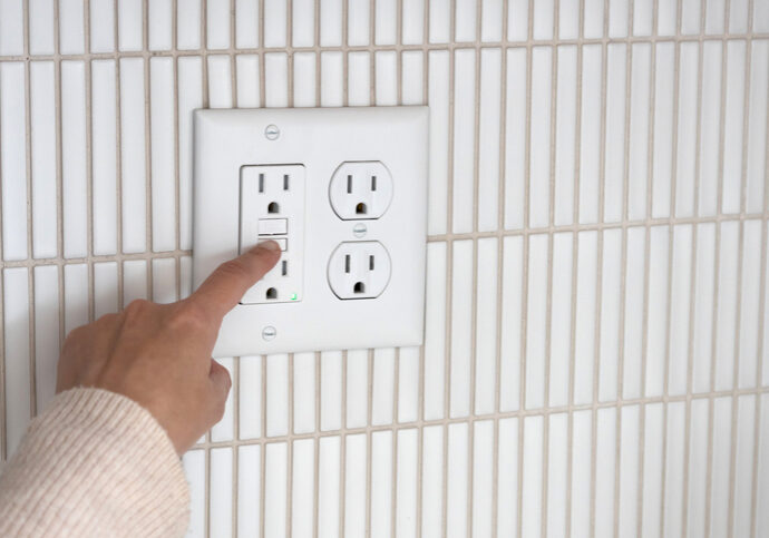 Person pressing a button on a wall-mounted outlet panel.