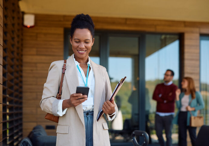 A professional woman checks her phone outside an office building.