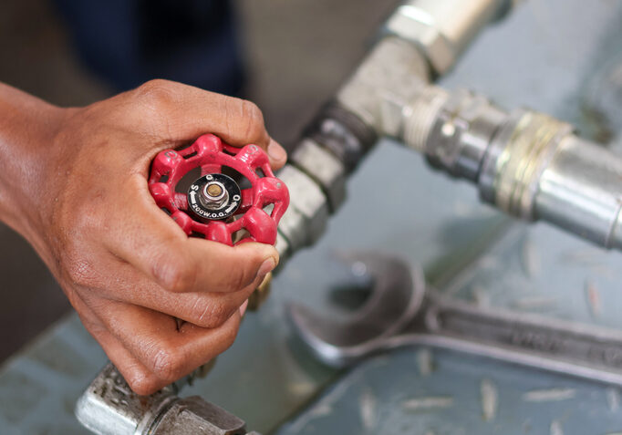 Hand turning a red valve on a metal pipe.
