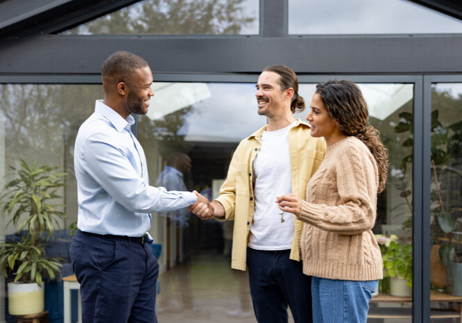 Two men shaking hands while a woman looks on, all smiling.