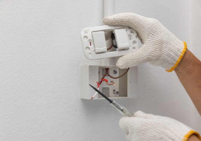 Person repairing a light switch with a screwdriver and wearing white gloves.