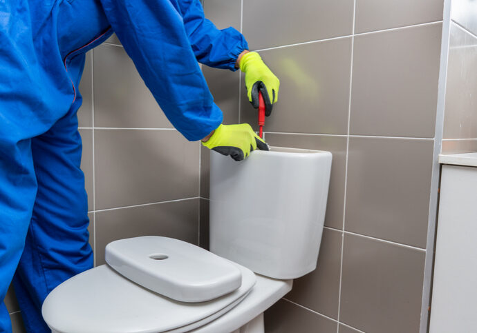 A person repairing a toilet tank with a screwdriver.