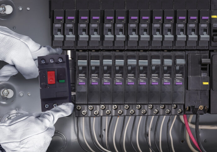 Hand operating a circuit breaker panel with multiple switches and wires.