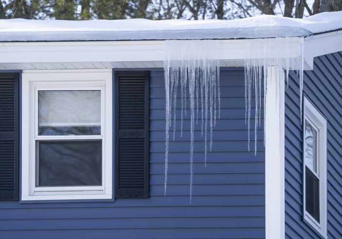 Long icicles hanging from a snowy roof over a window.