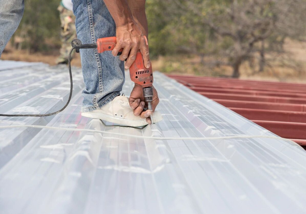 Person using an electric sander on a metal roof panel outdoors.