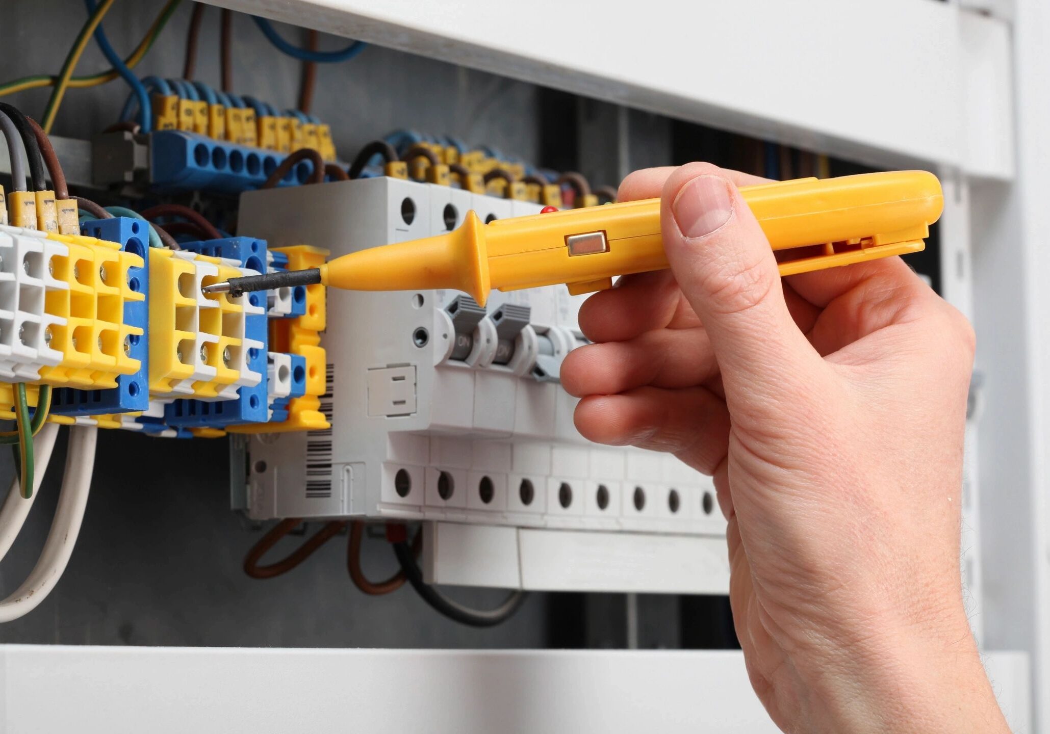 Hand using a voltage tester on an electrical panel.