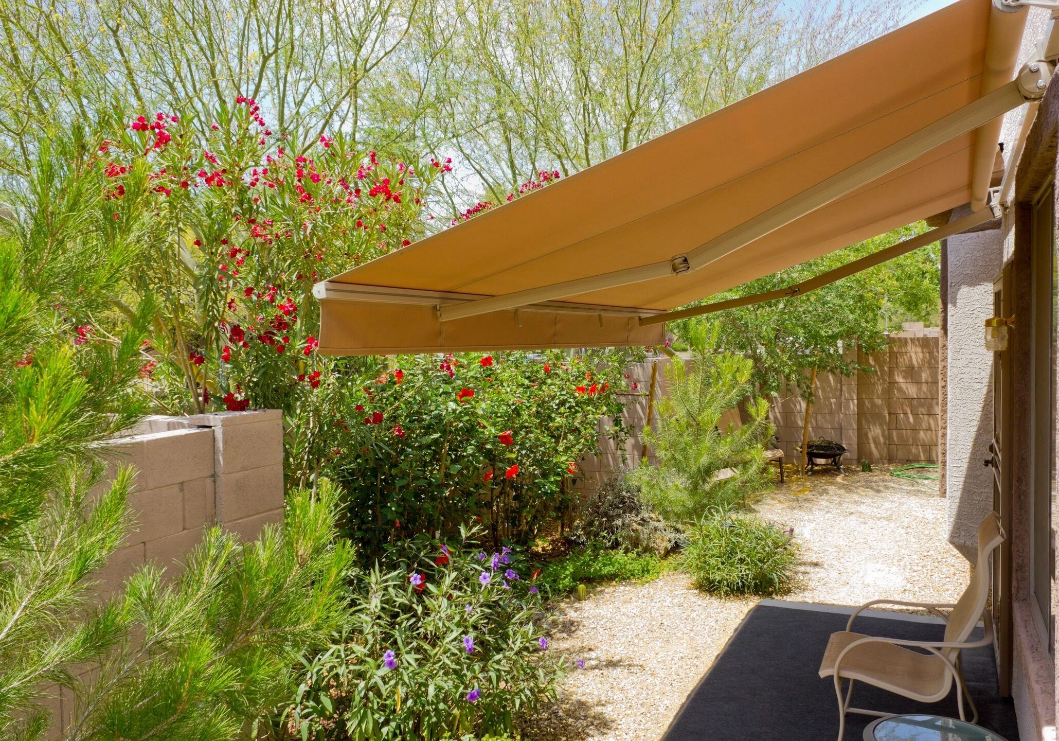 A sunny garden with vibrant plants and an orange awning providing shade.