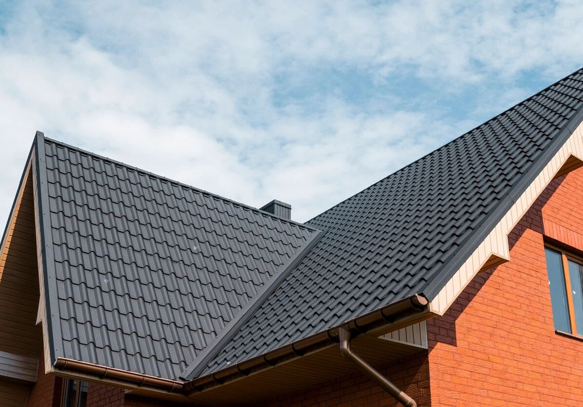 Modern house roof with dark tiles under a partly cloudy sky.