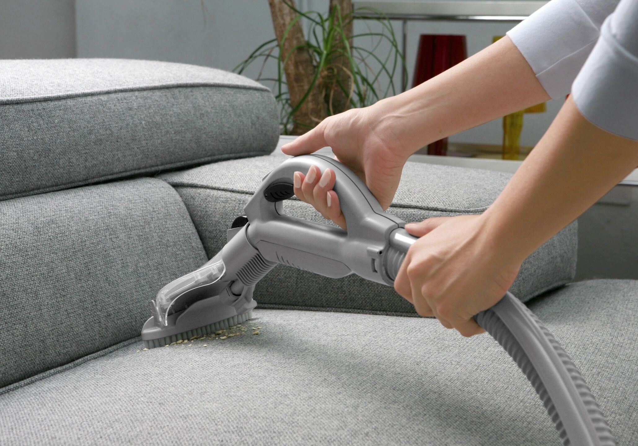 Person using a handheld vacuum to clean a sofa.