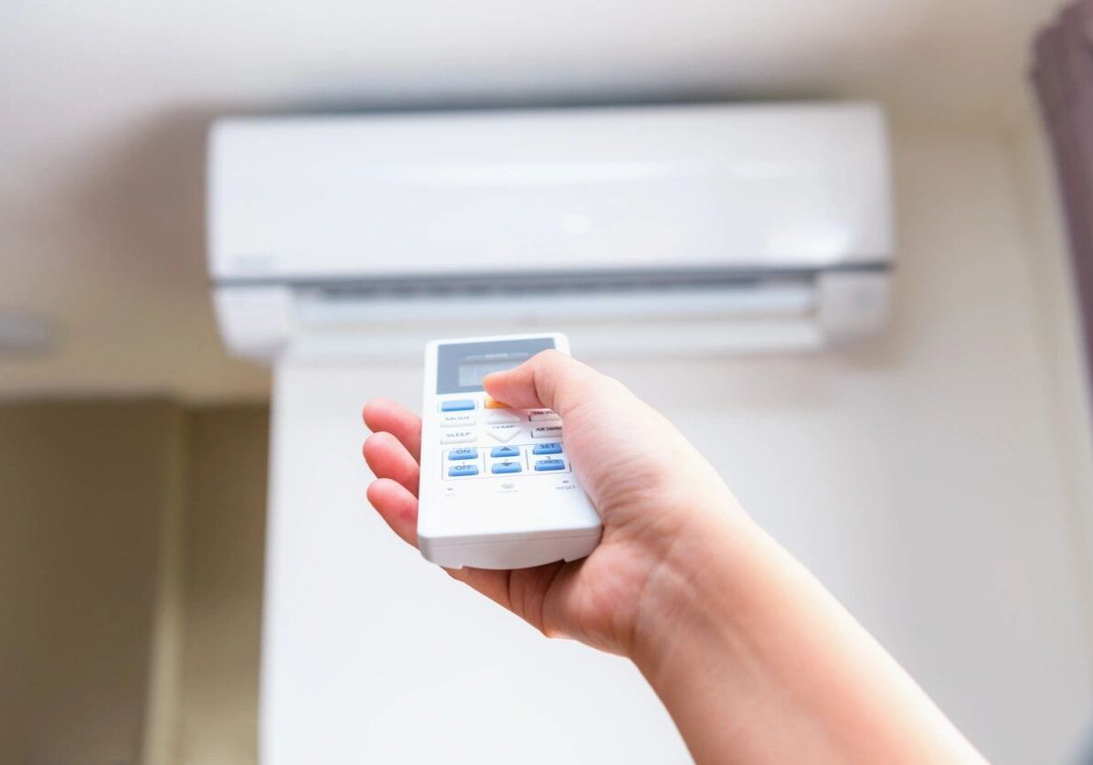 Hand holding remote controlling an air conditioner mounted on a wall.