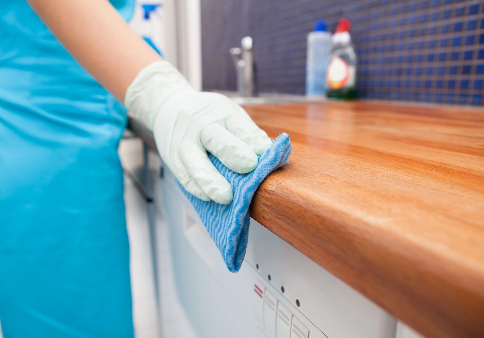 A person wearing gloves cleaning a wooden countertop with a blue cloth.
