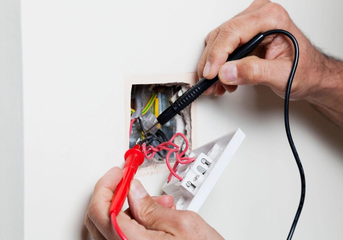 Hands wiring a junction box with tools and colored cables.