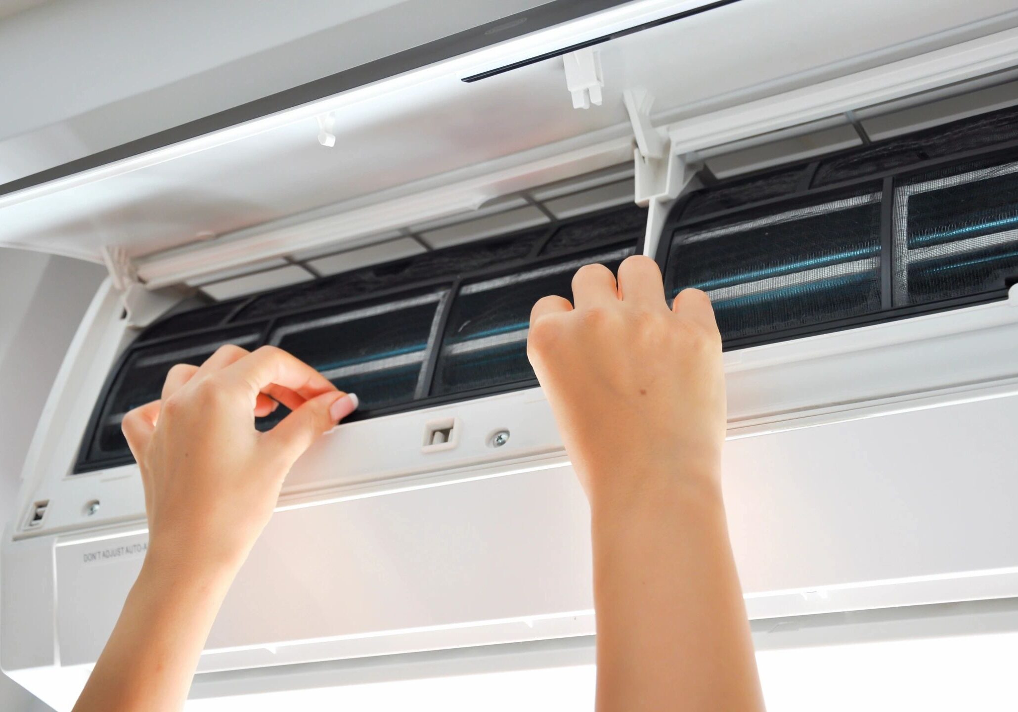 Hands cleaning an air conditioner filter with a brush.